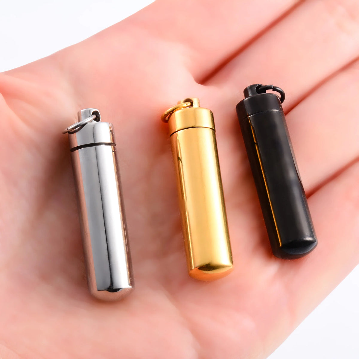 Stainless steel memorial pendants in silver, gold and black shown in the hand for size